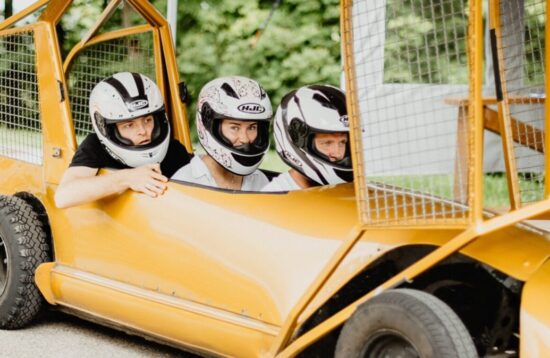 Smiling tourists wearing helmets in a summer bobsleigh on wheels in Sigulda.